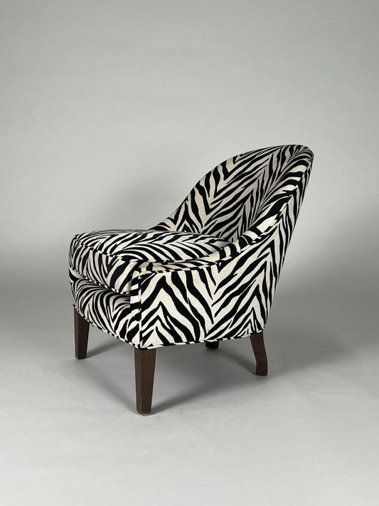 Black and white zebra patterned hair on hide chair with round back and brown legs.