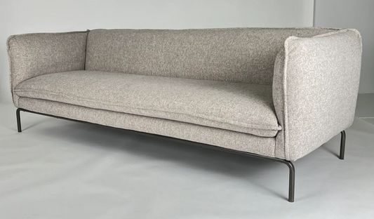 Neutral stone colored fabric sofa with curved iron base, flanged edges