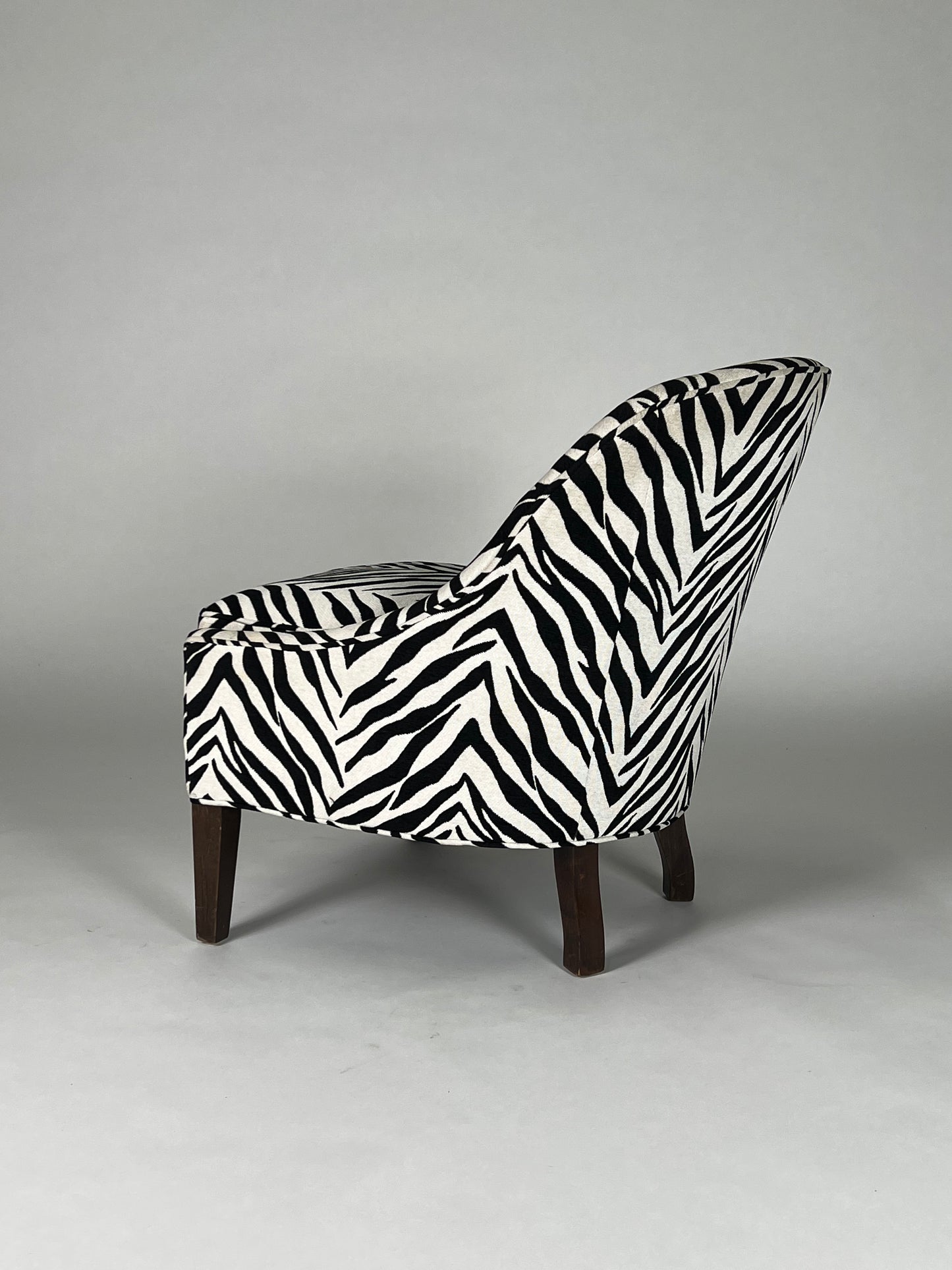 Black and white zebra patterned hair on hide chair with round back and brown legs.