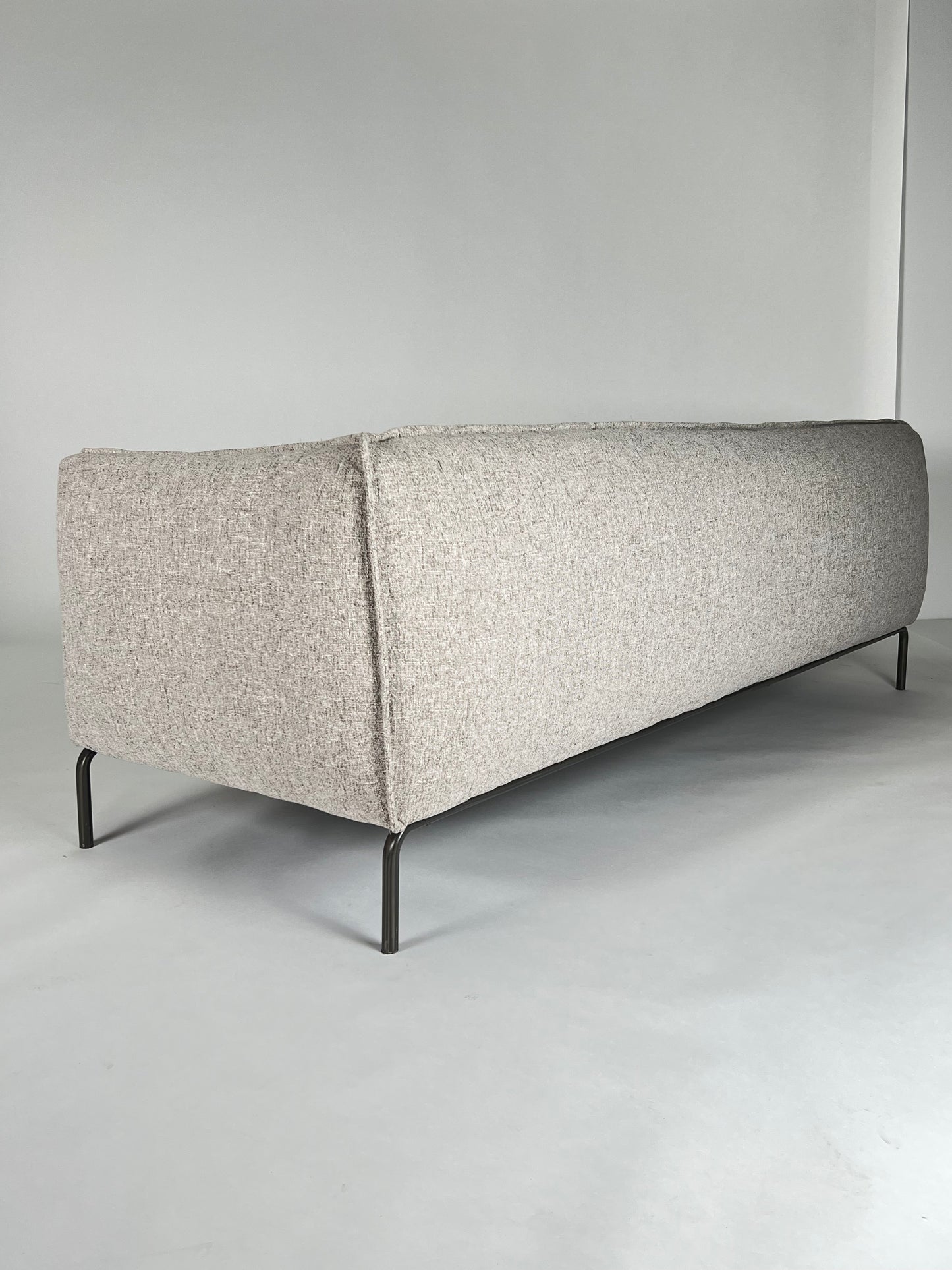 Neutral stone colored fabric sofa with curved iron base, flanged edges