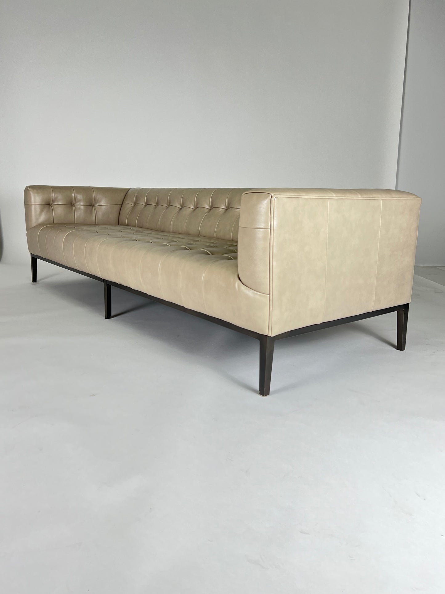 Buff colored leather sofa, squared off arms, blind tufting, gunmetal toned legs